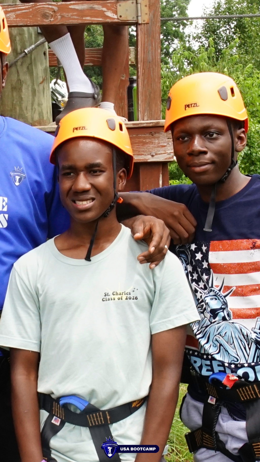 Two campers in climbing helmets and harnesses smiling together at the ropes course.