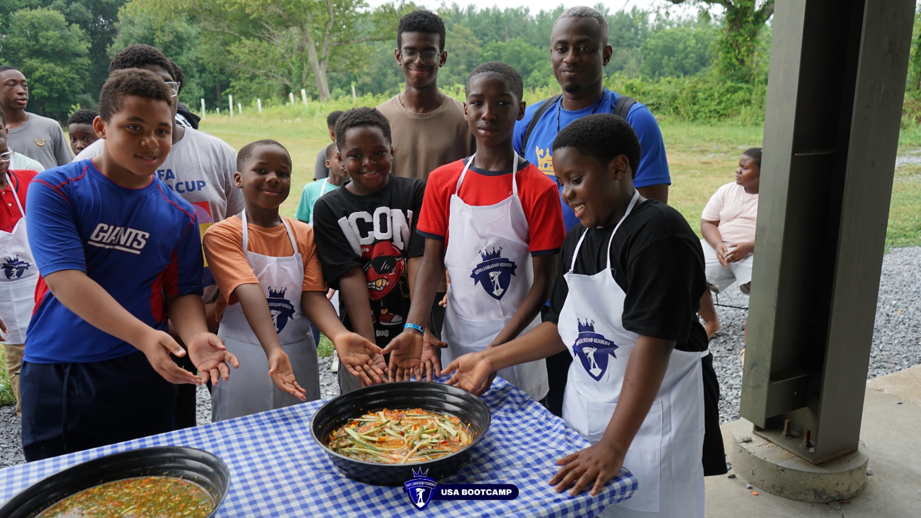 Boys in aprons gathered around a table of freshly cooked food.