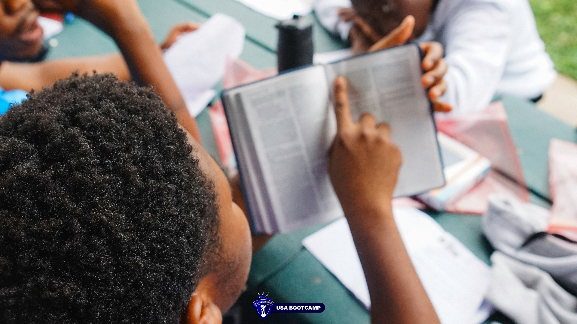 Boys studying scripture together at an outdoor table during boot camp.