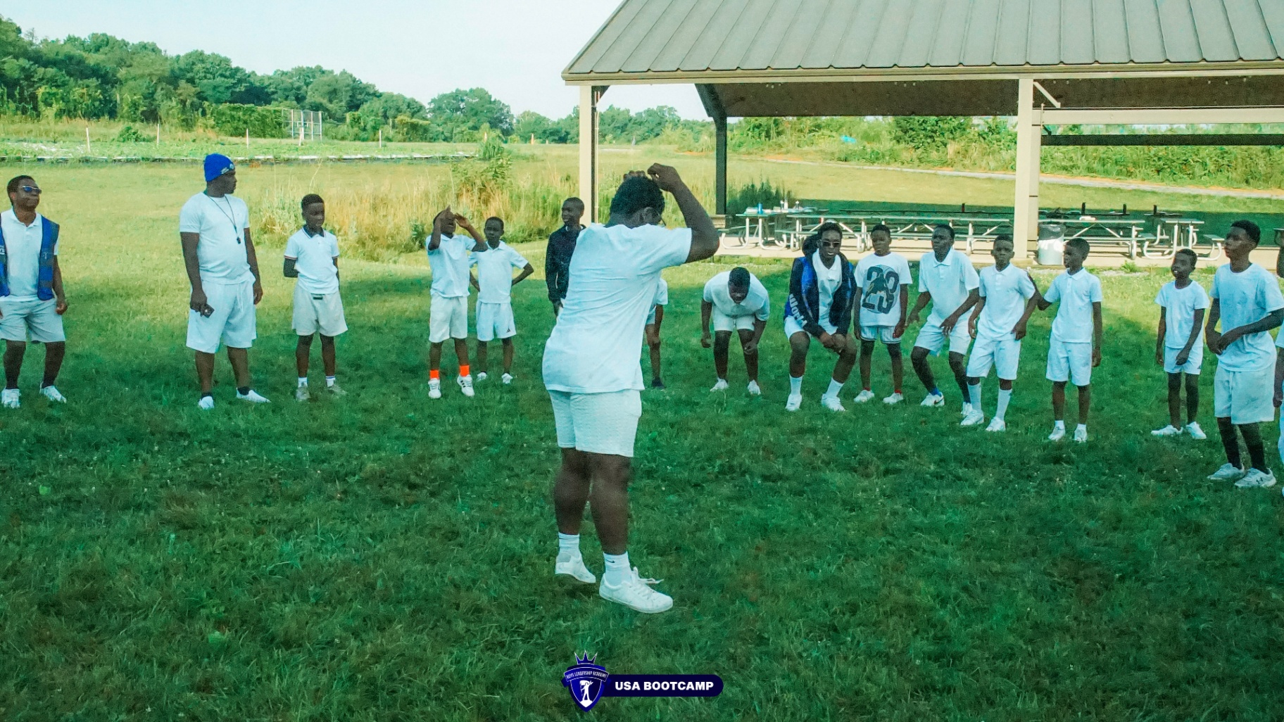 Boys in white uniforms lined up in a field for a drill.