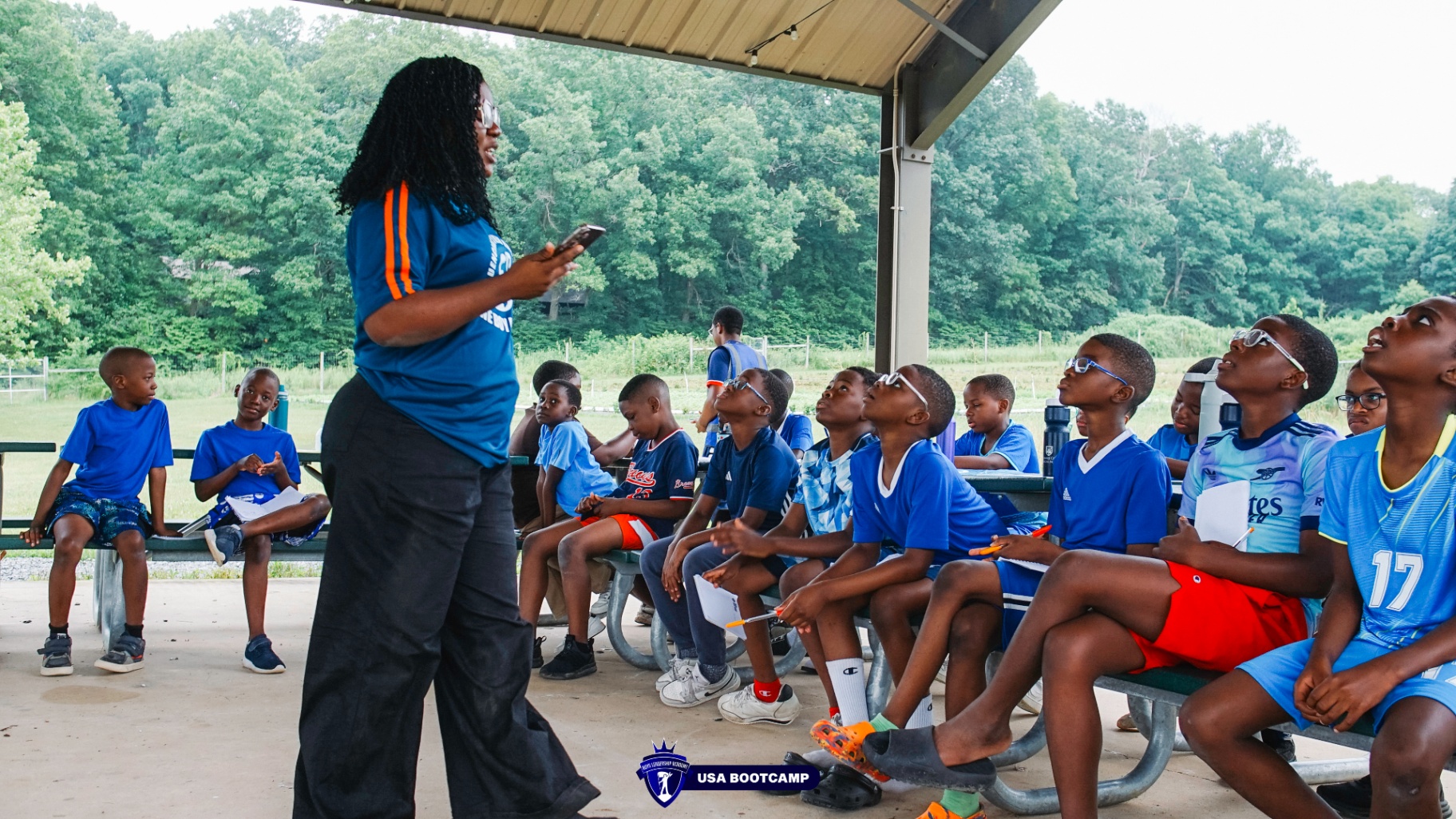 A mentor teaching a group of attentive boys under a pavilion.